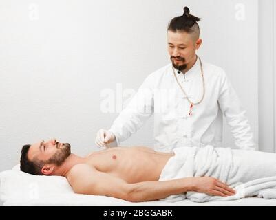 Acupuncturist insère des aiguilles d'acupuncture à des points spéciaux sur les méridiens du corps d'un homme. Médecine alternative, traitement des aiguilles Banque D'Images