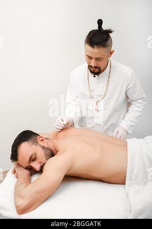 médecin faisant une acupuncture pour un patient pour traiter des maux de dos chroniques. Aiguille de gros plan pour l'acupuncture dans le dos de l'homme Banque D'Images