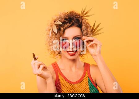 Rastafarian femme avec des feuilles de marijuana avec ses cheveux et lunettes élégantes tient un tuyau pour fumer du cannabis Banque D'Images