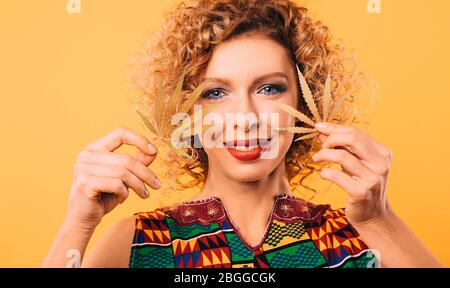 femme avec une coiffure curieuse et un sourire sur son visage tient des feuilles de marijuana dans ses mains. Légalisation du cannabis Banque D'Images