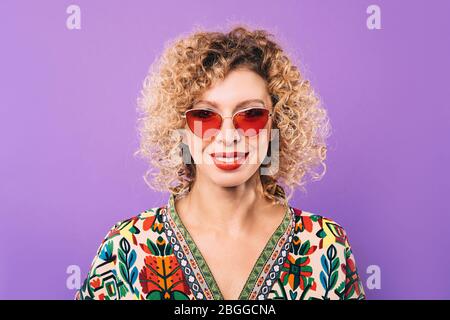 Portrait d'une femme dans des lunettes roses élégantes et une coiffure curly sur un fond violet. Beau sourire sur le visage d'une belle femme Banque D'Images