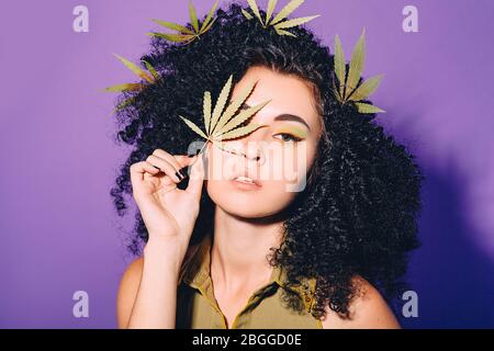 Portrait rastafarian femme avec feuille de cannabis près du visage. Légalisation de la marijuana. Face rapprochée sur fond violet Banque D'Images