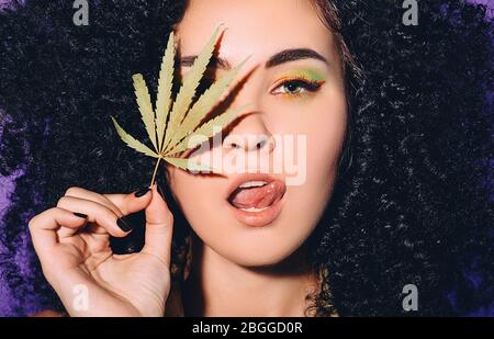 Portrait rastafarian femme avec feuille de cannabis près du visage. Légalisation de la marijuana. Face rapprochée sur fond violet Banque D'Images