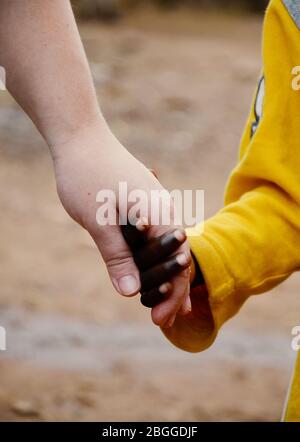 Gros plan sur l'enfant africain et la femme caucasienne qui tiennent les mains pacifiquement et très bien ensemble. Banque D'Images