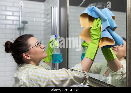 Miroir de nettoyage pour femme dans la salle de bains avec chiffon professionnel et spray de lavage, gros plan Banque D'Images