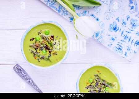 Soupe à la crème verte maison avec asperges, pois verts, graines de sésame noir et huile de citrouille sur fond blanc en bois Banque D'Images