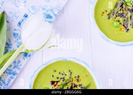 Soupe à la crème verte maison avec asperges, pois verts, graines de sésame noir et huile de citrouille sur fond blanc en bois Banque D'Images