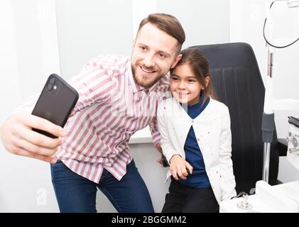 Papa et sa fille prennent un selfie dans le bureau de l'ophtalmologiste après examen des yeux. La vision de fille est très bonne Banque D'Images