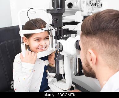 L'ophtalmologiste mâle vérifie la vue d'une petite fille à l'aide d'une lampe à fente binoculaire. Fille souriait parce que sa vue est très bonne Banque D'Images