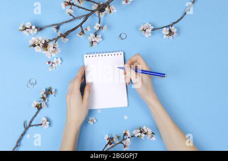Fille écrivant la liste de souhaits pour les plans futurs. composition de plat avec fleurs, bloc-notes. Planification de mariage Banque D'Images