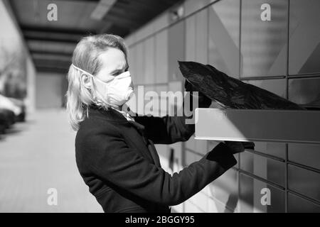 lady portant un masque de visage reçoit un colis ou un colis d'un terminal de post-colis à Tallinn. Femme portant un masque respiratoire de visage - protection contre Banque D'Images