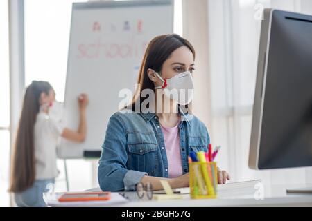 Femme dans le masque de protection à l'ordinateur, fille écrivant sur tableau noir. Banque D'Images