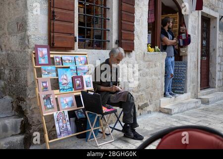 Monténégro, 17 septembre 2018 : un artiste se trouve à côté de ses peintures exposées dans la rue de la vieille ville de Kotor Banque D'Images