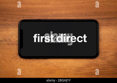 Un smartphone affichant le logo First Direct repose sur une table en bois ordinaire (usage éditorial uniquement). Banque D'Images