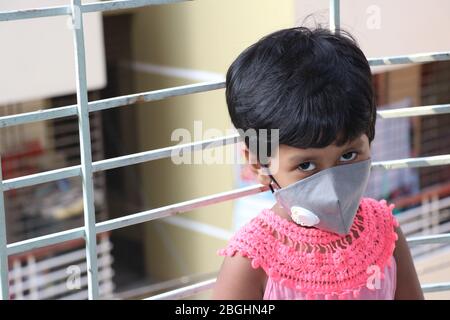 Passage d'un temps ennuyeux en raison de l'épidémie de virus Corona. Verrouillage et fermeture des écoles. Une fille d'école avec masque de visage regardant dehors par la fenêtre. Banque D'Images