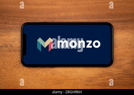 Un smartphone affichant le logo de la Banque Monzo repose sur une table en bois ordinaire (usage éditorial uniquement). Banque D'Images