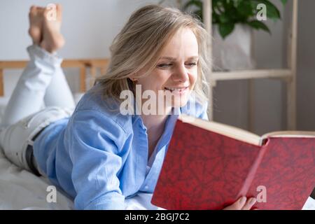 blonde femme tenant livre ouvert et lecture couché sur le lit. Loisirs, rester à la maison et quarantaine. Le temps pour vous Banque D'Images