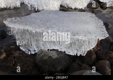 Gros plan du bloc de glace candled pendant la fonte printanière sur le rivage du fleuve Yukon, avec des roches et de l'eau Banque D'Images