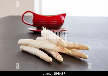 Asperges blanches brutes avec un bateau à sauce rouge en arrière-plan. Légumes frais sur table noire. Banque D'Images