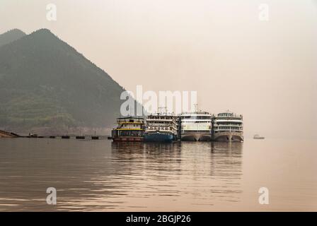 Fengdu, Chine - 8 mai 2010: Coup de matin sur l'eau brune Yangtze River sous brouillard et ciel smog sur 4 bateaux de passagers amarrés au pont ponton de termina Banque D'Images