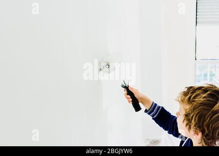 Garçon aide sa famille à peindre un mur blanc. Banque D'Images