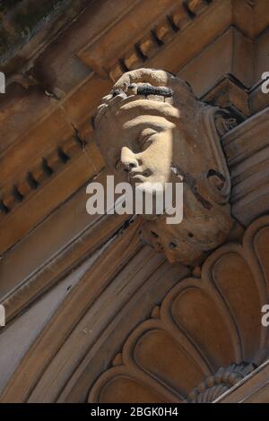 Gros plan sur un visage sculpté ensoleillé au sommet d'une voûte plantaire sur un bâtiment en grès blond victorien très orné à Glasgow, en Écosse. Diagonales. Banque D'Images