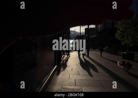 Concept « lumière au bout du tunnel ». Plusieurs personnes en silhouette jettent de longues ombres sur un trottoir dans une section rétroéclairé d'une rue à Glasgow. Banque D'Images