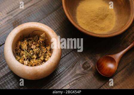 Mortier de marbre avec camomille séchée pour cosmétiques naturels. Bol en argile avec poudre jaune ou argile et fleurs sur fond en bois. Pose plate. Banque D'Images