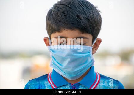 Jeune garçon indien portant un masque médical blanc. Mise au point sur la partie avant du visage yeux fermés, flou de fond. Coronavirus, COVID-19 Banque D'Images