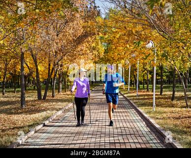 Jeune couple en formation automne parc. L'homme est le jogging et la femme faisant de la marche nordique avec des bâtons. Concept de vie en bonne santé. Banque D'Images