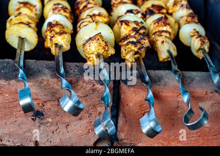 Barbecue sur des brochettes de métal poli au sommet de briques rouges brûlées. Gros-plan de kabobs de poulet grillé maison avec oignons frais. Banque D'Images