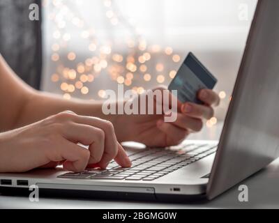 Ok computer magasinage en ligne soncept. Close-up woman's hands holding credit card, et saisie des informations de carte à l'aide du clavier d'ordinateur portable pour faire des achats en ligne avec l'éclairage festif de flou de la chaîne. Banque D'Images