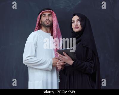 jeune homme d'affaires musulman arabe avec femme en robe hijab tendance utilisant téléphone mobile et tablette ordinateur devant un représentant noir de tableau de surveillance Banque D'Images