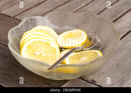 Un bol en verre rempli de quartiers de citron se tient sur une table en bois. Avec la cuillère, les tranches sont placées dans de l'eau rafraîchissante ou de la limonade. Banque D'Images