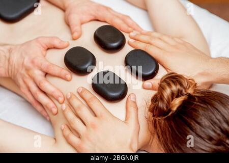 Les mains de massothérapeutes font des massages de dos tandis que des pierres chaudes à l'arrière de la femme près dans le spa. Banque D'Images