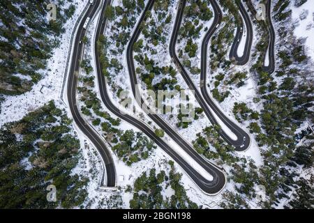 Vue aérienne d'une voiture en serpentin sur une montagne. Route vers le village et le domaine skiable de la Thuile. Serpentine de montagne enneigée dans la vallée d'Aoste en Italie. Banque D'Images