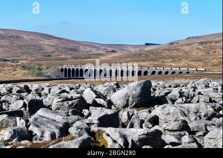 Le train transportant la pierre de la carrière Arcow traverse Ribblehead Viaduc, Yorkshire Dales National Park, Royaume-Uni. Pavé calcaire au premier plan. Banque D'Images