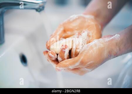 Une personne se lave soigneusement les mains avec du savon et de la mousse sur l'évier, à partir du robinet dont l'eau coule dans un ruisseau. Banque D'Images