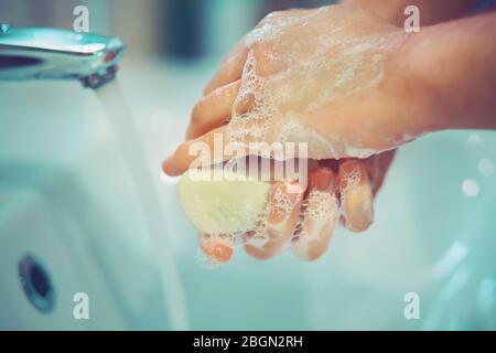Un homme tient un savon blanc et se lave les mains avec lui, et contre le fond de l'eau du robinet coule dans l'évier. Banque D'Images