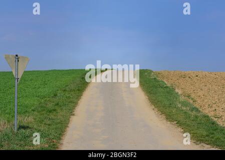 En Bavière, une route pavée étroite traverse la campagne à travers les zones agricoles, avec un ciel bleu et un panneau de signalisation derrière Banque D'Images