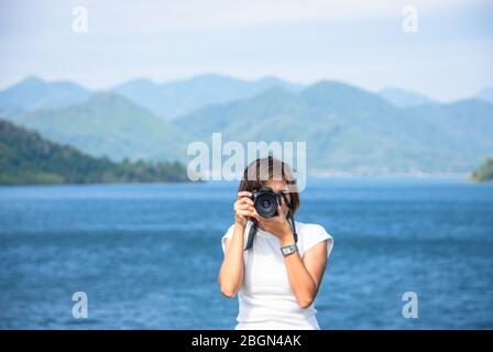 Main femme tenant l'appareil photo prendre des photos fond Kaeng Krachan Dam phetchaburi , Thaïlande. Banque D'Images