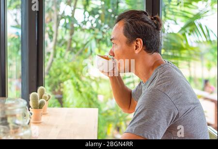 Homme asiatique tenant une tasse de café à la main et boire fond cactus mis sur la table. Banque D'Images