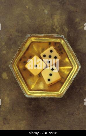 Petite boîte hexagonale en laiton contenant trois dés anciens indiquant les numéros 1 et 3 et 5 Banque D'Images