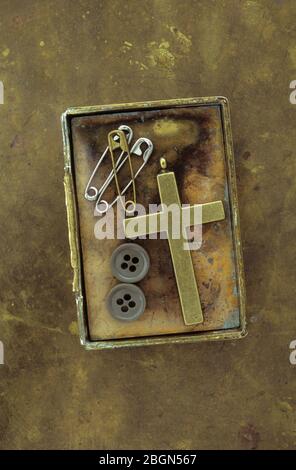 Boîte en laiton vintage contenant un crucifix en laiton ancien trois goupilles de sécurité utilisées et deux boutons mâles Banque D'Images