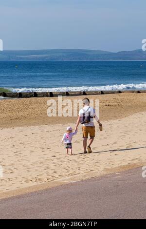 Bournemouth, Dorset, Royaume-Uni. 22 avril 2020. Météo au Royaume-Uni : belle journée chaude et ensoleillée, les températures montent sur les plages de Bournemouth sur la côte sud, les gens s'exerçant avec leur autorisation, en respectant la plupart des directives du coronavirus. Homme et tout-petit marchant sur la plage. Crédit : Carolyn Jenkins/Alay Live News Banque D'Images