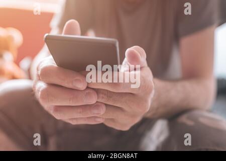 Homme utilisant le téléphone mobile à la maison, gros plan sur les mains des hommes accro au smartphone, mise au point sélective Banque D'Images