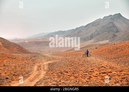Man on mountain bike en chemise bleue dans le désert rouge Banque D'Images