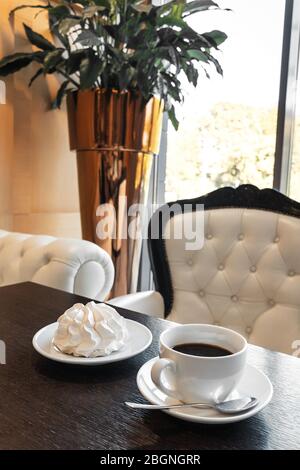 Tasse de café noir avec meringue sur une table texturée en bois sombre dans un café à l'intérieur classique. Gros plan. Banque D'Images