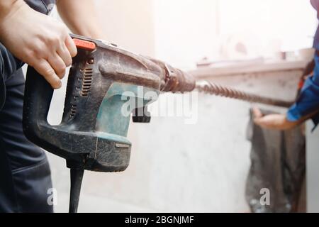 Homme ouvrier du constructeur avec équipement perforateur de marteau perforateur faisant trou dans la construction de mur gris Banque D'Images