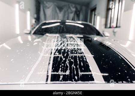 Voiture blanche sport de luxe moderne recouverte de mousse. Lavage de voiture. Gros plan photo de la hotte de voiture dans le service de lavage de voiture à l'intérieur Banque D'Images